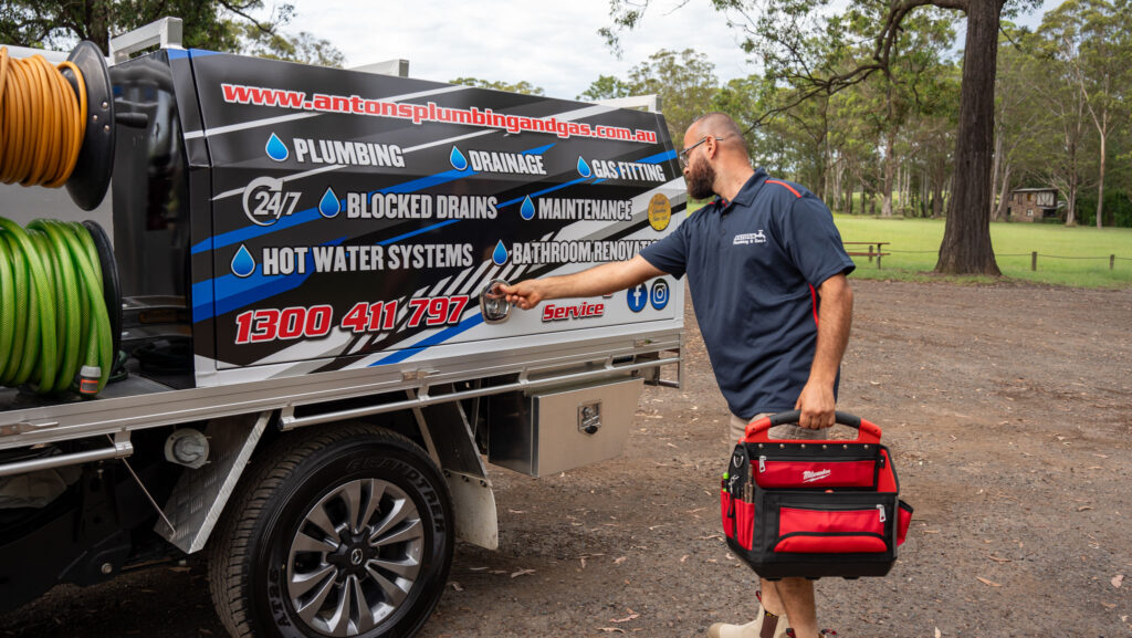 A professional plumber from Anton's Plumbing works on a shower fixture, highlighting expertise in servicing hot water systems.